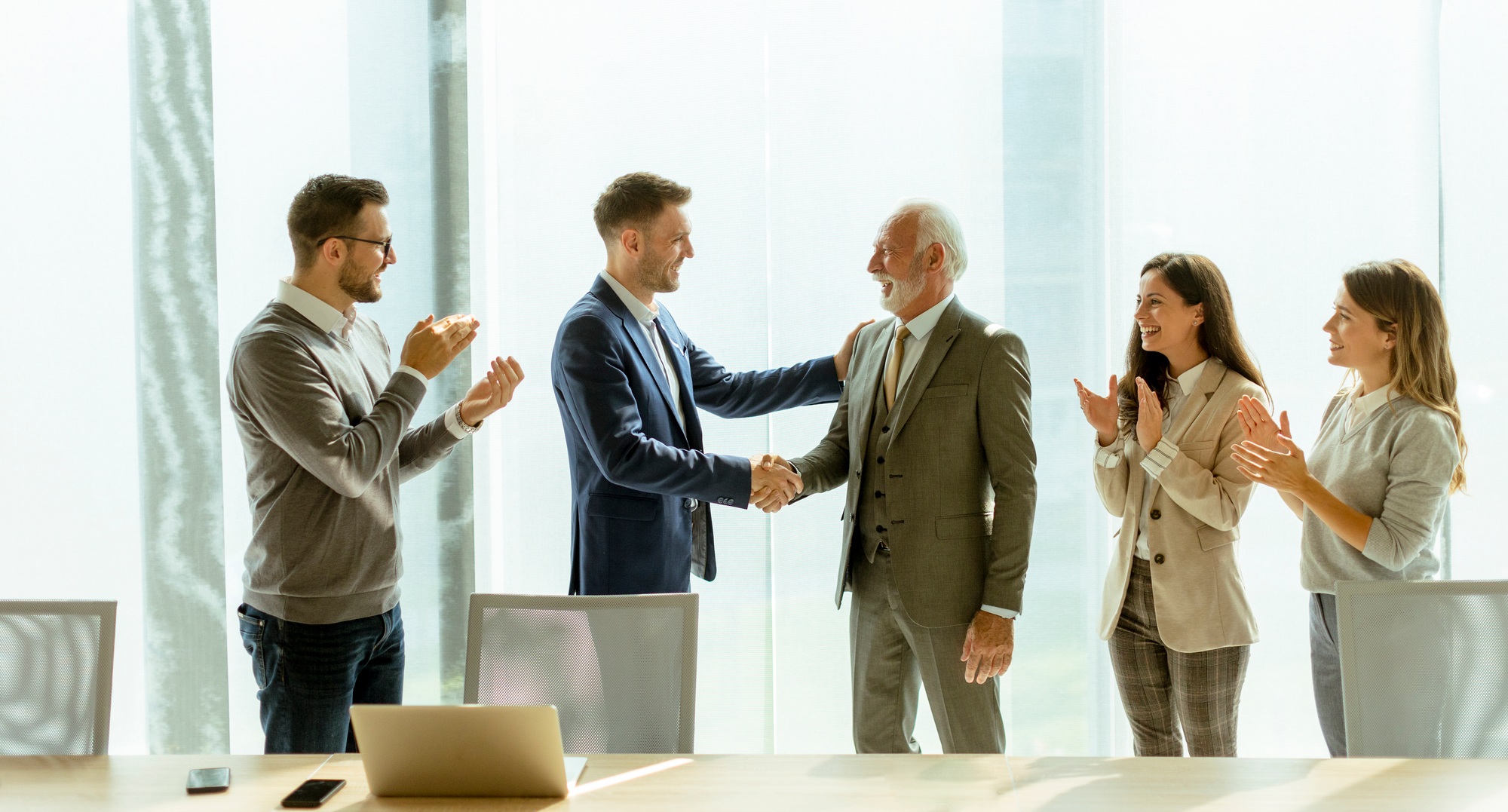 Business partners handshaking after making agreement with employees near by